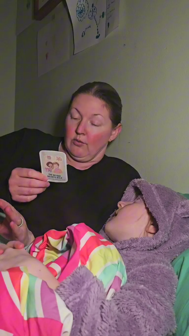 A mom reading the No Bad Secrets Rule card to her child at bedtime